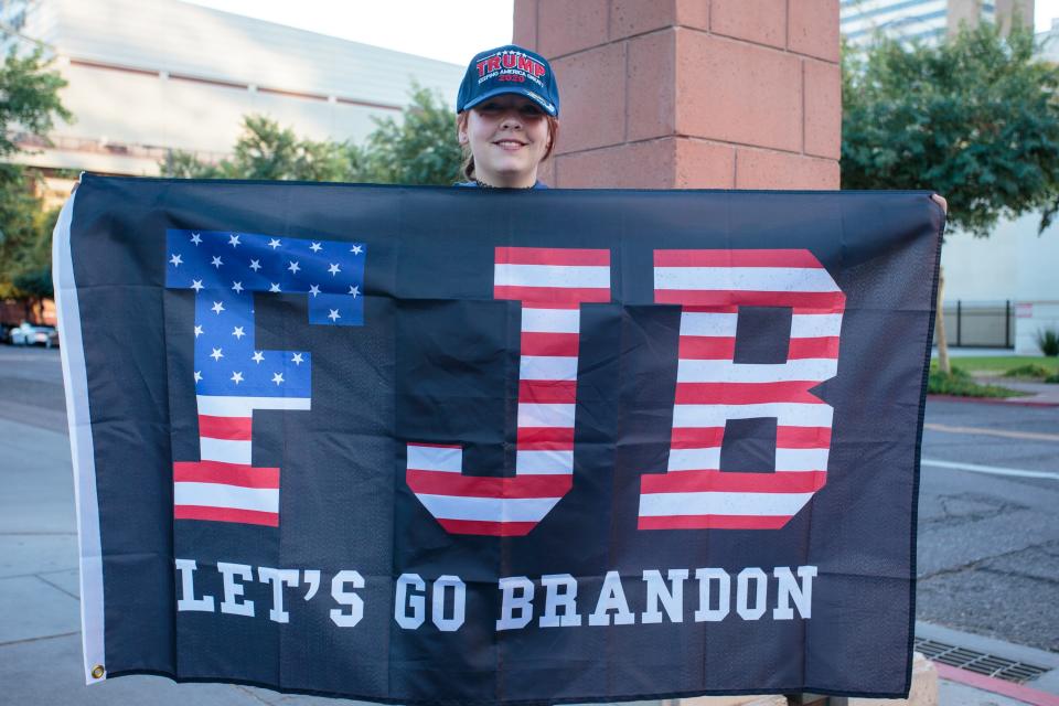 Rhoanna Streeter holds a flag reading "F JB, Let's Go Brandon" at the intersection of Third and Van Buren streets near the Phoenix Convention Center on Day 2 of Turning Point USA's AmericaFest 2021 on Dec. 19, 2021.