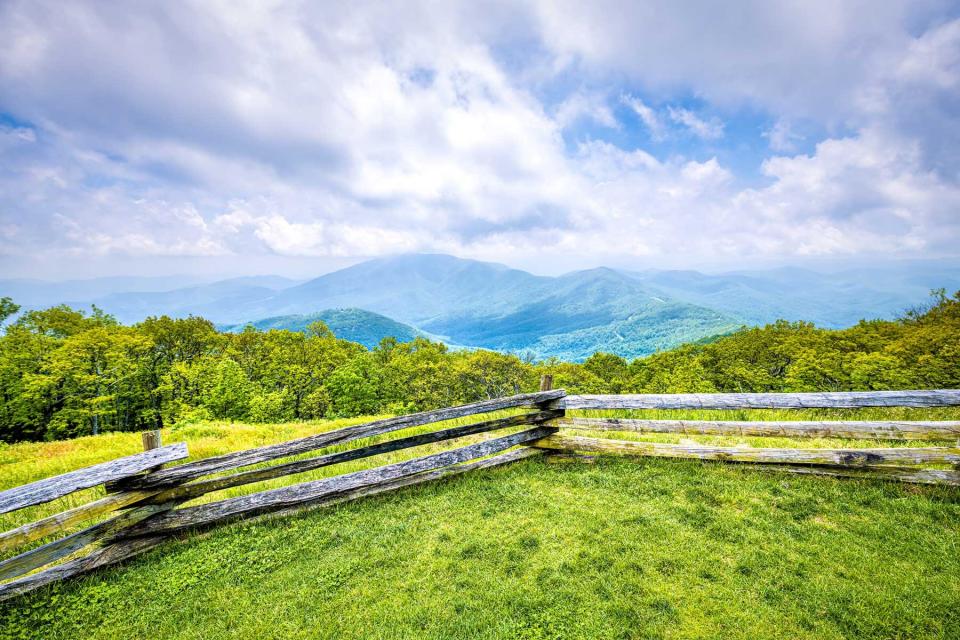 Devil's Knob Overlook with fence and green grass field meadow at Wintergreen resort town village in Blue Ridge mountains in summer clouds mist fog