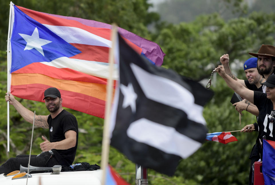 Puerto Rican singer Ricky Martin holds a Puerto Rico flag as he participates in a protest demanding the resignation of governor Ricardo Rossello, in San Juan, Puerto Rico, Friday, July 19, 2019. Protesters are demanding Rossello step down for his involvement in a private chat in which he used profanities to describe an ex-New York City councilwoman and a federal control board overseeing the island's finance. (AP Photo/Carlos Giusti)