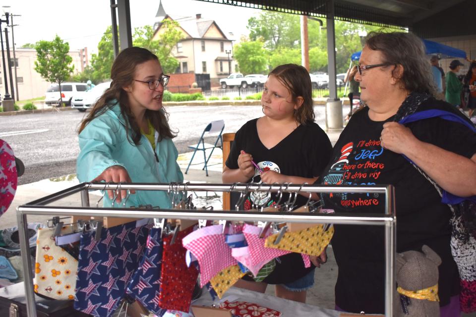 Local crafter Elizabeth Gall, left, talks about her business, Elizabeth's Handmade Designs, and its offerings to Roxanne Cummings, right, and Cierra Corbin, 10, both of Adrian during Saturday's grand opening of the Adrian City Market at the Pavilion in downtown Adrian. Gall, of Morenci, said her fabric and clothing business is in its second year.