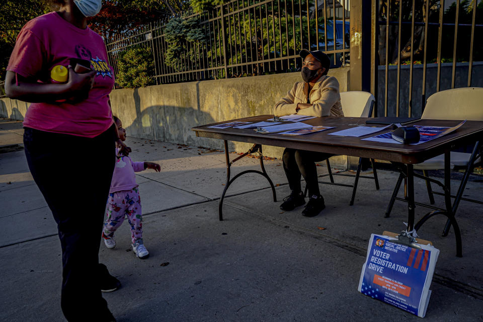 A woman and child walk past Laurae Caruth, right, volunteer with Christian Cultural Center Social Justice Initiative's voter registration drive, as she sits at a table where she registers voters, Friday, Sept. 18, 2020, in the Brooklyn borough of New York. "I'm out here volunteering because of how important it is to exercise the right to vote," Caruth said. In recent election cycles, predominantly Black congregations across the country have launched get-out-the-vote campaigns commonly referred to as “souls to the polls.” But instead of packing buses and vans to shuttle people to early voting sites this year, church leaders say they are organizing caravans for absentee ballot drop-offs and in-person early voting. (AP Photo/Bebeto Matthews)