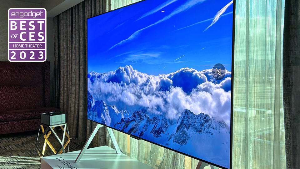 An angled view of the 97-inch LG M3 OLED with wireless tech sitting in a hotel room in front of a translucent window curtain.