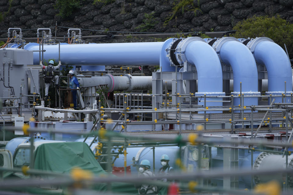 People work by a blue pipeline to transport seawater, part of the facility for the release of treated radioactive water to sea from the Fukushima Daiichi nuclear power plant, operated by Tokyo Electric Power Company Holdings, also known as TEPCO, in Futaba town, northeastern Japan, Friday, July 14, 2023. (AP Photo/Hiro Komae)