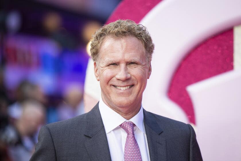 Will Ferrell in a grey suit wearing a pink tie smiling at a red carpet premiere for Barbie