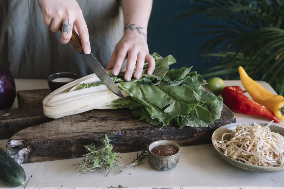 Frau schneidet Pak Choi mit großem Messer. 