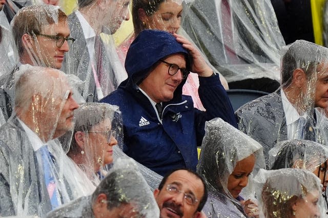 Prime Minister Sir Keir Starmer, wearing just a coat, is in the crowd at the Paris opening ceremony surrounded by officials wearing waterproof ponchos. 