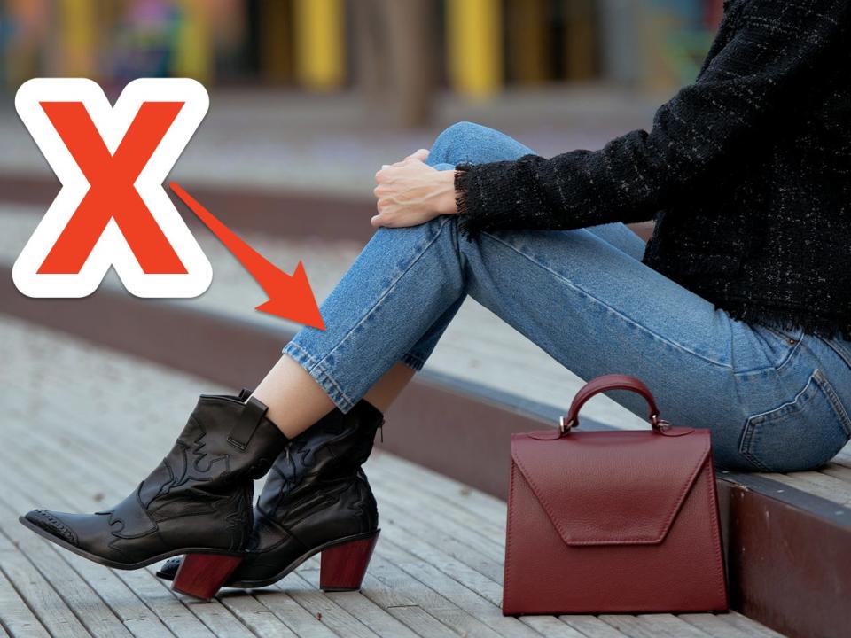 red x and arrow pointing at woman's blue ankle skinny jeans as she sits outside on steps