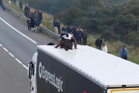 Groups of migrants gather on the road as two board a lorry on the access road to reach the ferry terminal in Calais, France, October 3, 2015. REUTERS/Pascal Rossignol