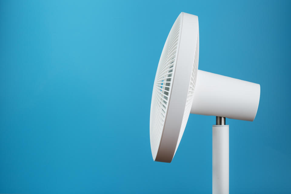 White modern electric fan for cooling the room on a blue background. Free space, minimalistic style.