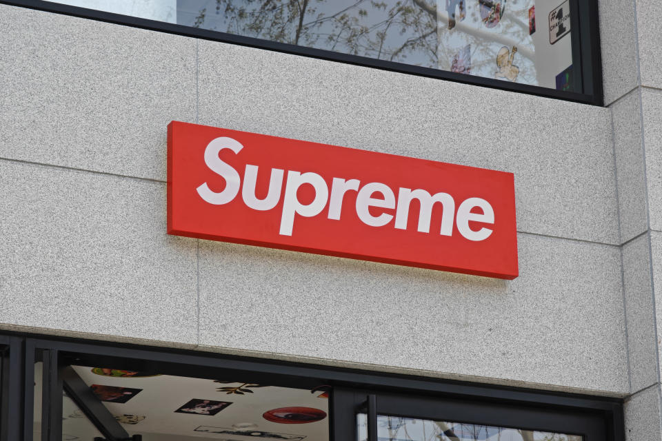 A sign with the brand name "Supreme" is mounted on the exterior of a building, positioned above a doorway