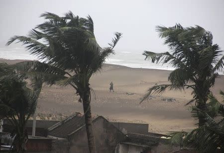 A man walks as strong winds blow along a beach in Gopalpur in Ganjam district in Odisha October 12, 2014. REUTERS/Stringer
