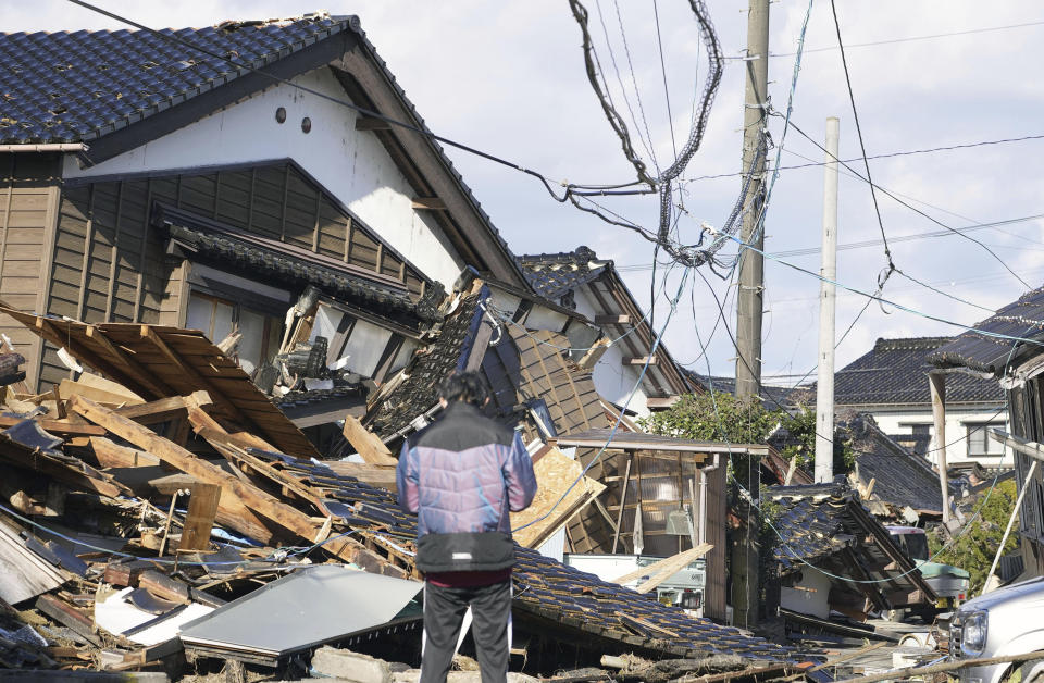 A man stands in front of a fallen house caused by earthquakes in Suzu, Ishikawa prefecture, Japan Thursday, Jan. 4, 2024. More soldiers have been ordered to bolster the rescue operations Thursday, providing those in need with drinking water, hot meals and setting up bathing facilities after a magnitude 7.6 quake hit Ishikawa Prefecture and nearby regions Monday. (Kyodo News via AP)