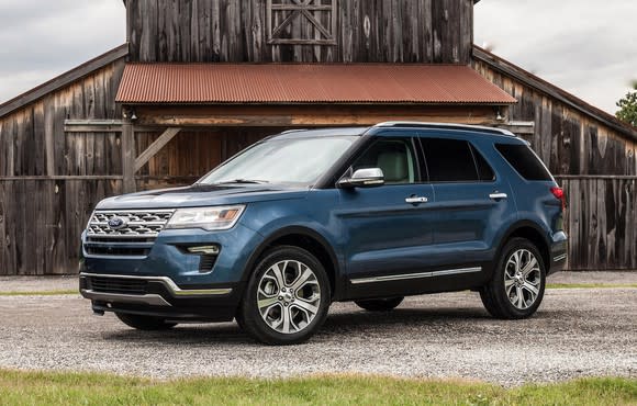 A blue Ford Explorer, a midsize crossover SUV, parked in front of a barn.