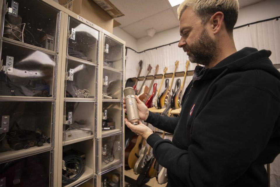 Man holding vintage microphone, a rack of guitars on the wall behind him