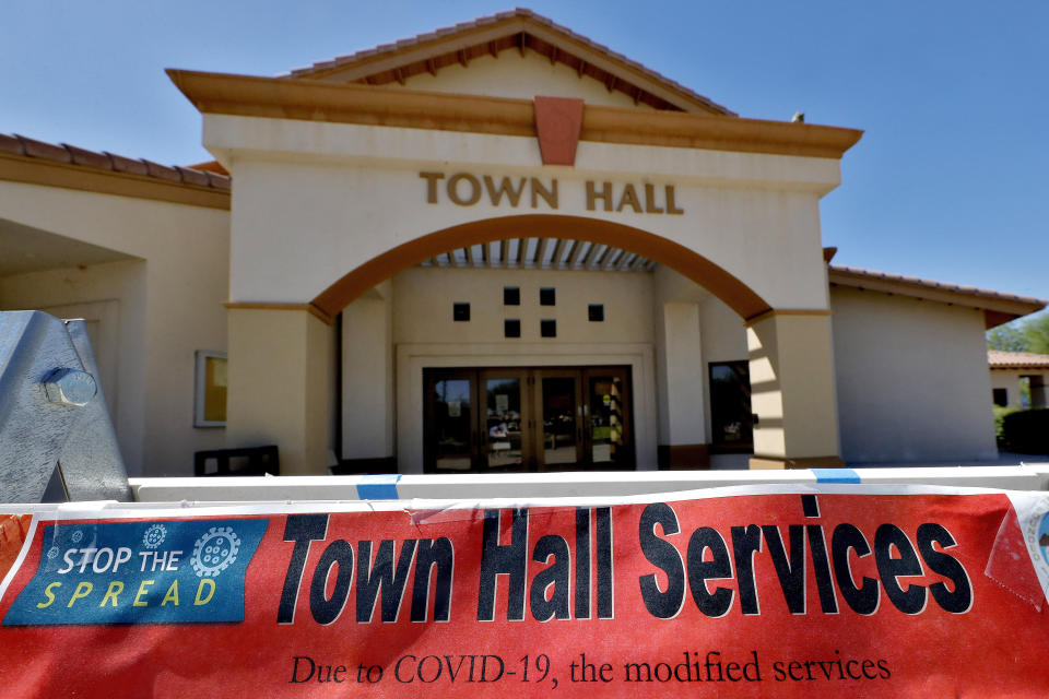 In this Thursday, June 18, 2020, photo, a sign in front of the Guadalupe Town Hall notifies visitors of modified services in Guadalupe, Ariz. As the coronavirus spreads deeper across America, it's ravaging through the homes and communities of Latinos from the suburbs of the nation's capital to the farm fields of Florida to the sprawling suburbs of Phoenix and countless communities in between. (AP Photo/Matt York)