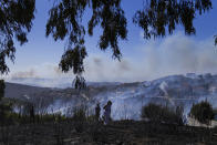 A woman walks in front of smoke from a fire in the area of Drafi , east of Athens on Wednesday, July 20, 2022. Hundreds of people were evacuated from their homes late Tuesday as a wildfire threatened mountainside suburbs northeast of Athens. Firefighters battled through the night, struggling to contain the blaze which was being intensified by strong gusts of wind. (AP Photo/Thanassis Stavrakis)