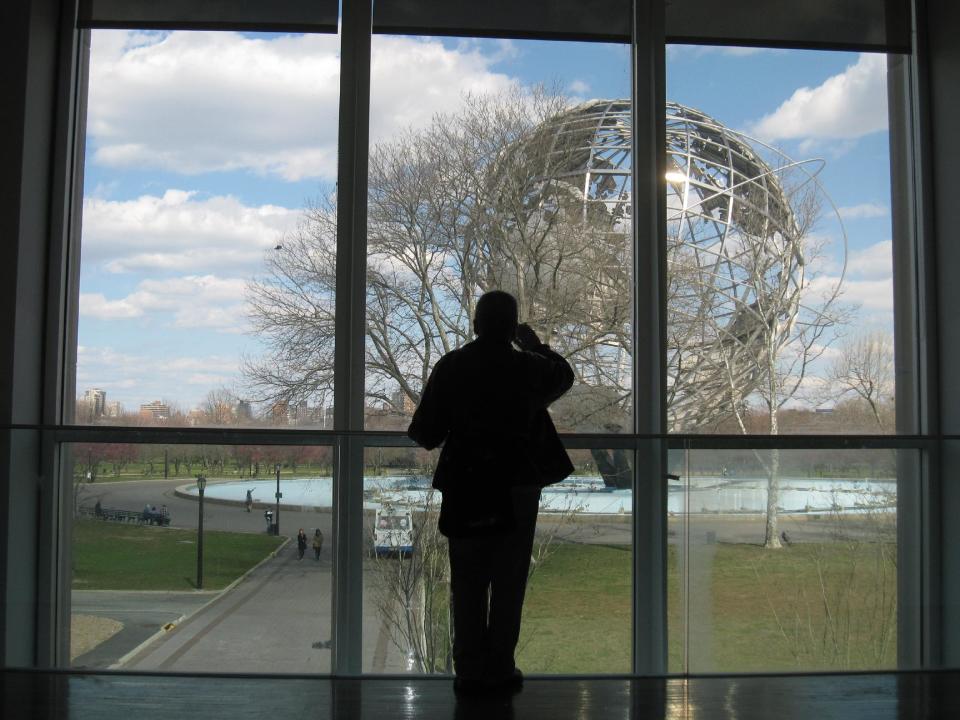 In this April 9, 2014, photo, a visitor to the Queens Museum of Art takes a photo of the Unisphere through the museum windows in the Queens borough of New York. The 12-story steel globe that debuted 50 years ago at the 1964 World’s Fair is one of a number of World’s Fair sites that can still be seen today. (AP Photo/Beth J. Harpaz)