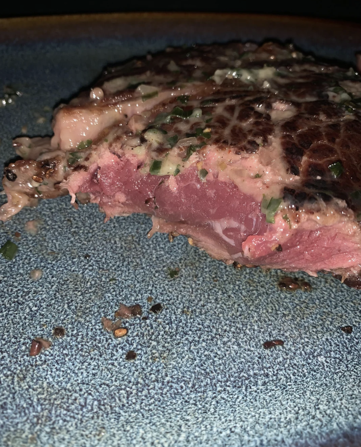 A close-up of a medium-rare steak seasoned with herbs on a plate