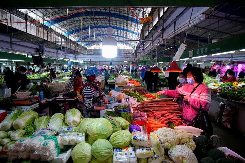 FILE PHOTO: People wearing face masks buy vegetables at a wet market, following an outbreak of the coronavirus disease (COVID-19) in Wuhan