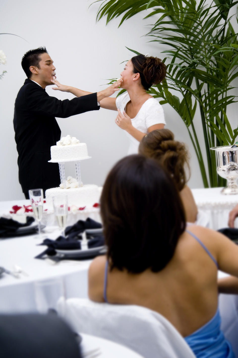 A groom and bride put wedding cake on each other's faces at their wedding reception