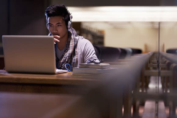 Student at desk studying on his laptop with headphones on.