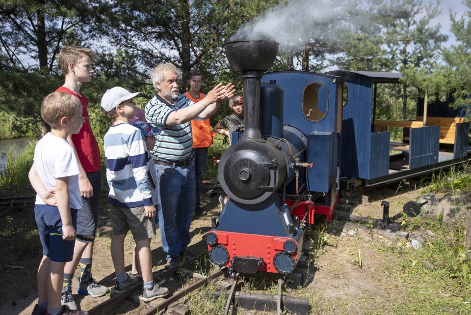 Pavel Chilin explains to children how his steam locomotive runs along his miniature personal railway in Ulyanovka village outside St. Petersburg, Russia Sunday, July 19, 2020. It took Chilin more than 10 years to build the 350-meter-long miniature personal narrow-gauge railway complete with various branches, dead ends, circuit loops, and even three bridges.(AP Photo/Dmitri Lovetsky)