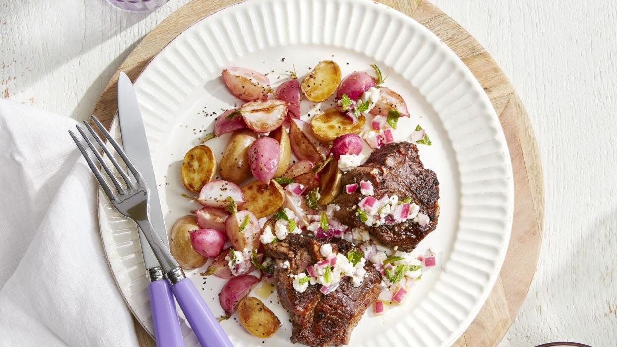 lamb chops with roasted potatoes and radishes on a white plate with silverware and a small bowl of relish on the side