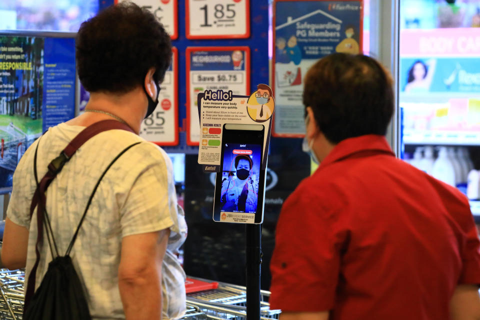 SINGAPORE - JUNE 19:  A woman wearing a protective mask has her temperature taken using a contactless temperature scanner before checking-in at a supermarket on June 19, 2020 in Singapore. Today, Singapore starts to further ease the coronavirus (COVID-19) restrictions by allowing social gatherings up to five people, re-opening of retail outlets and dining in at food and beverage outlets, subjected to safe distancing. Parks, beaches, sports amenities and public facilities in the housing estates will also reopen. However, large scale events, religious congregations, libraries, galleries and theaters will remain closed.  (Photo by Suhaimi Abdullah/Getty Images)