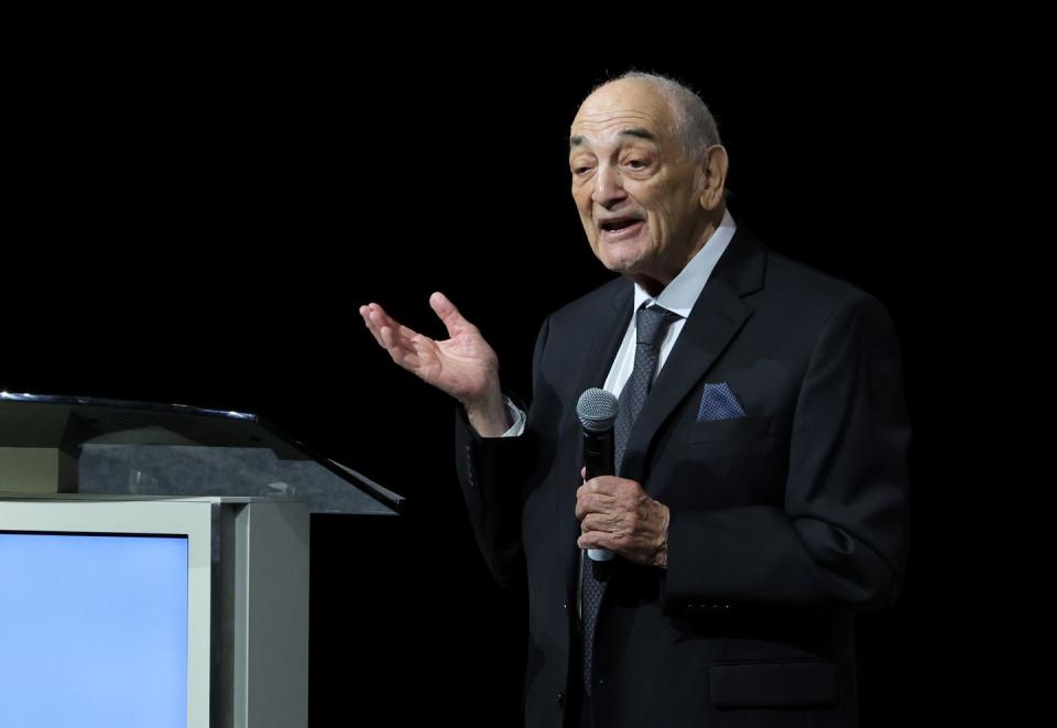 sonny vaccaro wearing a black suit and speaking into a microphone at a podium