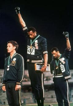 Two athletes with fists raised in protest standing on Olympic podium.