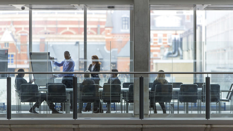 Group of six business people in a boardroom meeting. Shot at a distance from outside through the glass.