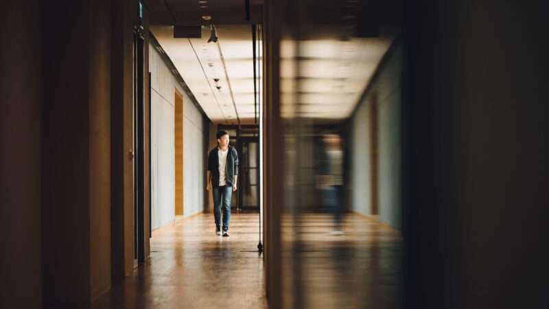 Teen walking down school hallway next to blurry mirror image of teen walking down school hallway
