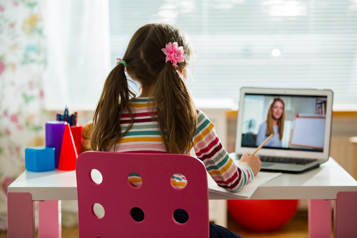 A young girl sits at a desk as she listens to her teacher during an online lesson.