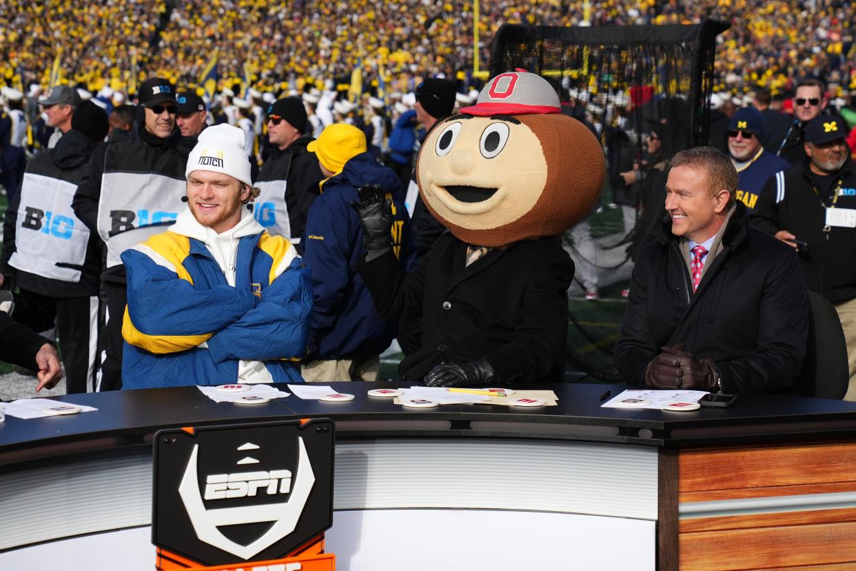 Nov 25, 2023; Ann Arbor, Michigan, USA; Lee Corso puts on a Brutus Buckeye head betwen Kirk Herbstreit and Aidan Hutchinson on the ESPN College Gameday set prior to the NCAA football game between the Michigan Wolverines and the Ohio State Buckeyes at Michigan Stadium.