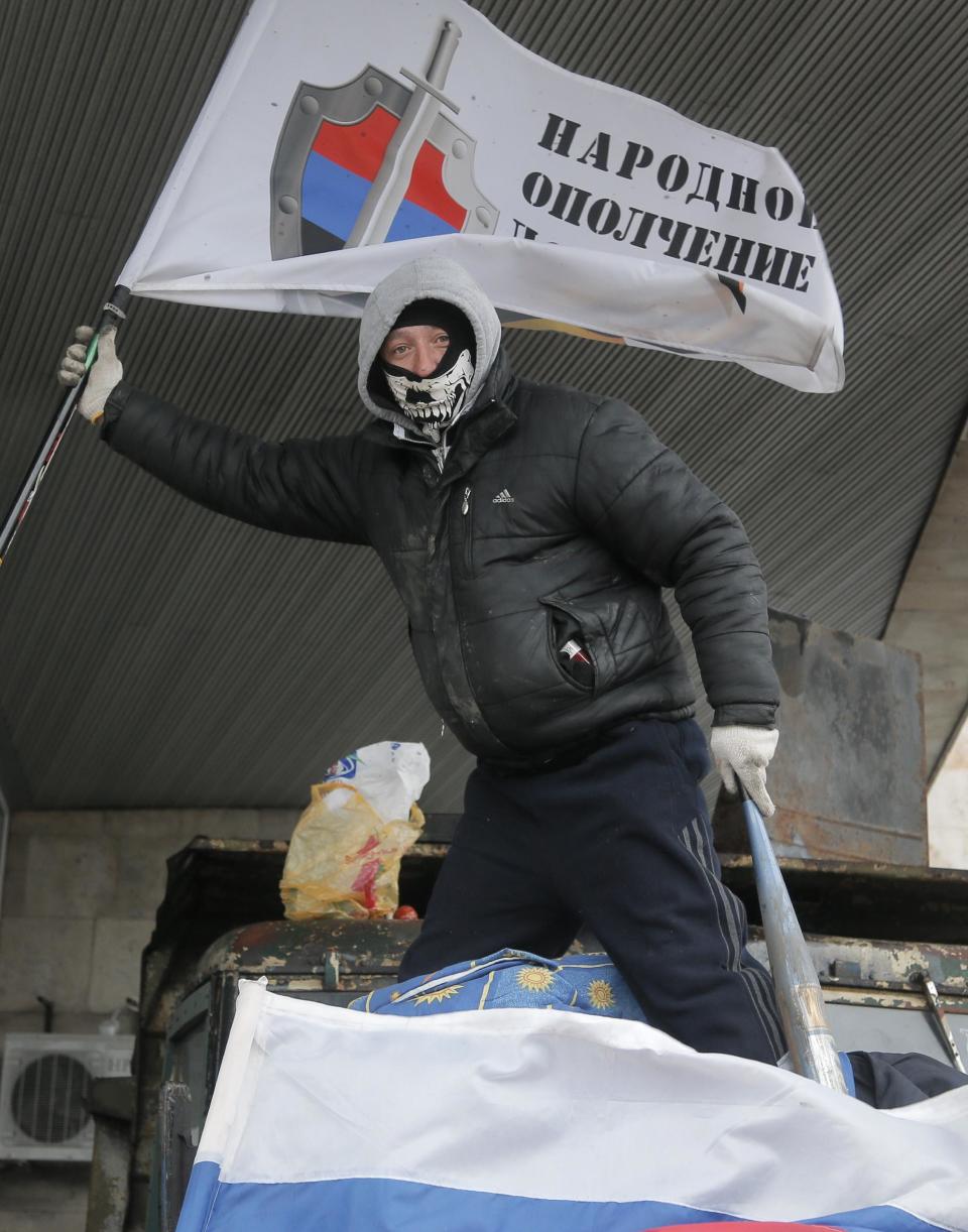 A masked pro-Russian activist holds up a flag on top of a barricade as he guards a regional administration building that they had seized earlier in Donetsk, Ukraine, Friday, April 11, 2014. The text on the flag reads: 'Militia of Donbass'. Ukraine’s prime minister on Friday told leaders in the country’s restive east that he is committed to allowing regions to have more powers. Yatsenyuk Friday morning flew into Donetsk, where pro-Russian separatists are occupying the regional administration building and calling for a referendum that could prefigure seeking annexation by Russia. (AP Photo/Efrem Lukatsky)