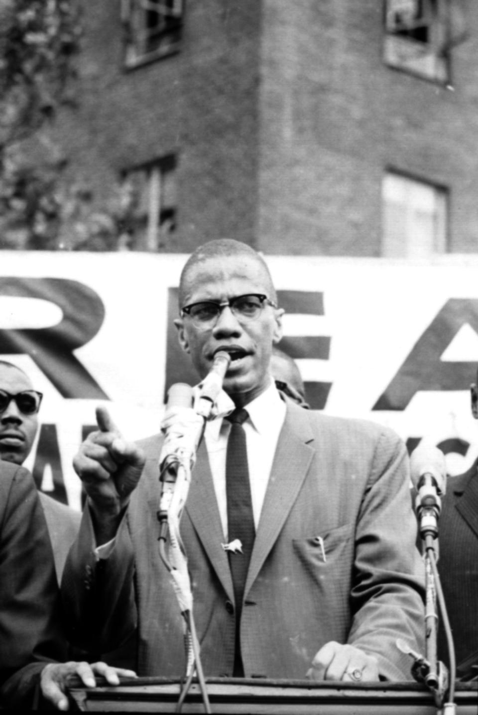 Black Nationalist ldr. Malcolm X at podium during rally w. others in bkgrd.   Malcolm X was later assassinated on February 21, 1965, by members of the Nation of Islam.