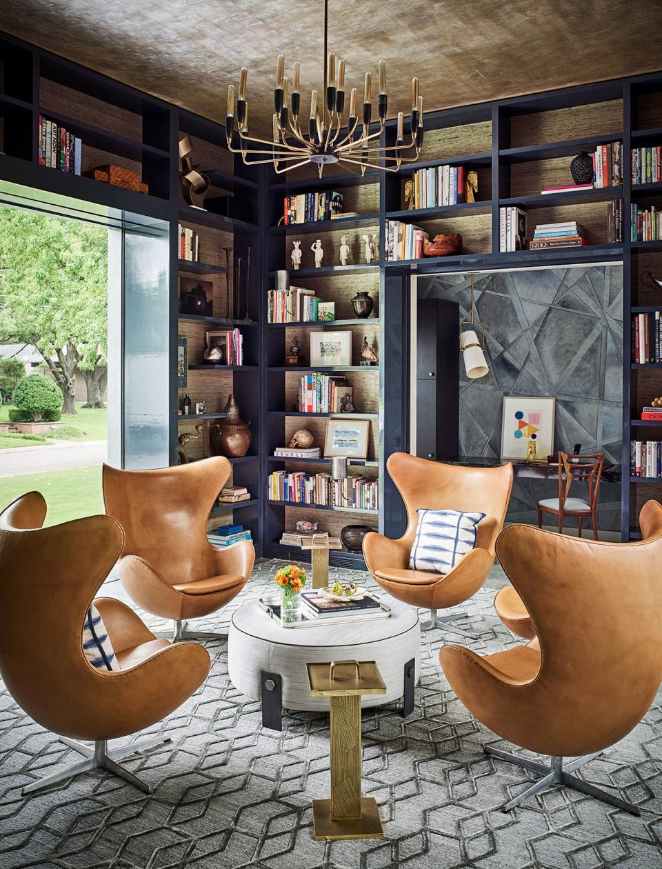 SHM Architects and designer Jay Jeffers collaborated on the Dallas home of Juliette and Mark Moussa, the founder of Arteriors (arteriorshome.com); the chandelier and accent tables are by Arteriors, the chairs are vintage Arne Jacobsen, and the bookcases are backed in Phillip Jeffries wallpaper.