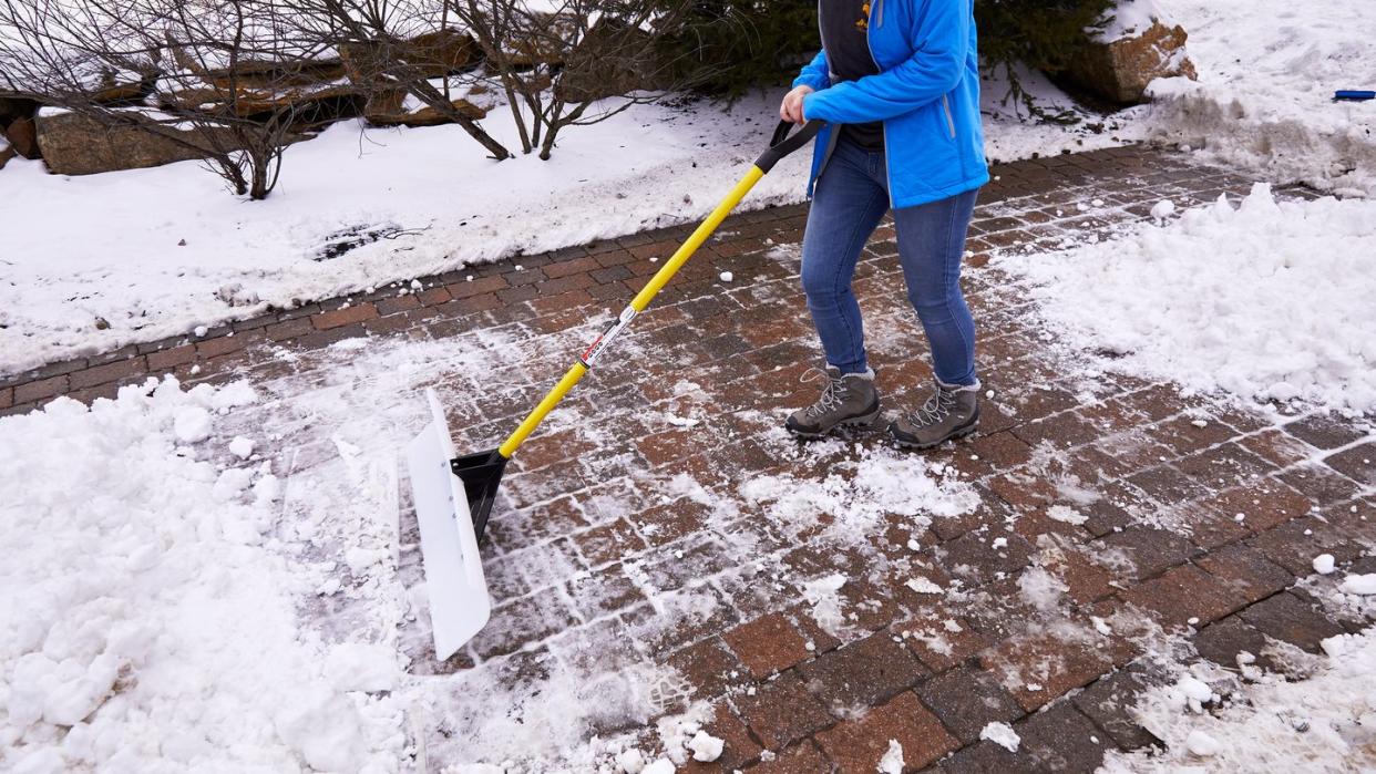 woman pushing snow shovel on brick patio