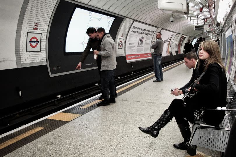 This is a late evening scene on the platform of Liverpool Street Underground Station in London. There are two young men observing mice on the tracks. A young lady is staring off into the distance. Another young man is sitting hunched over in contemplation. Another man in the distance is watching the men mouse-spotting. Taken on November 19, 2010.