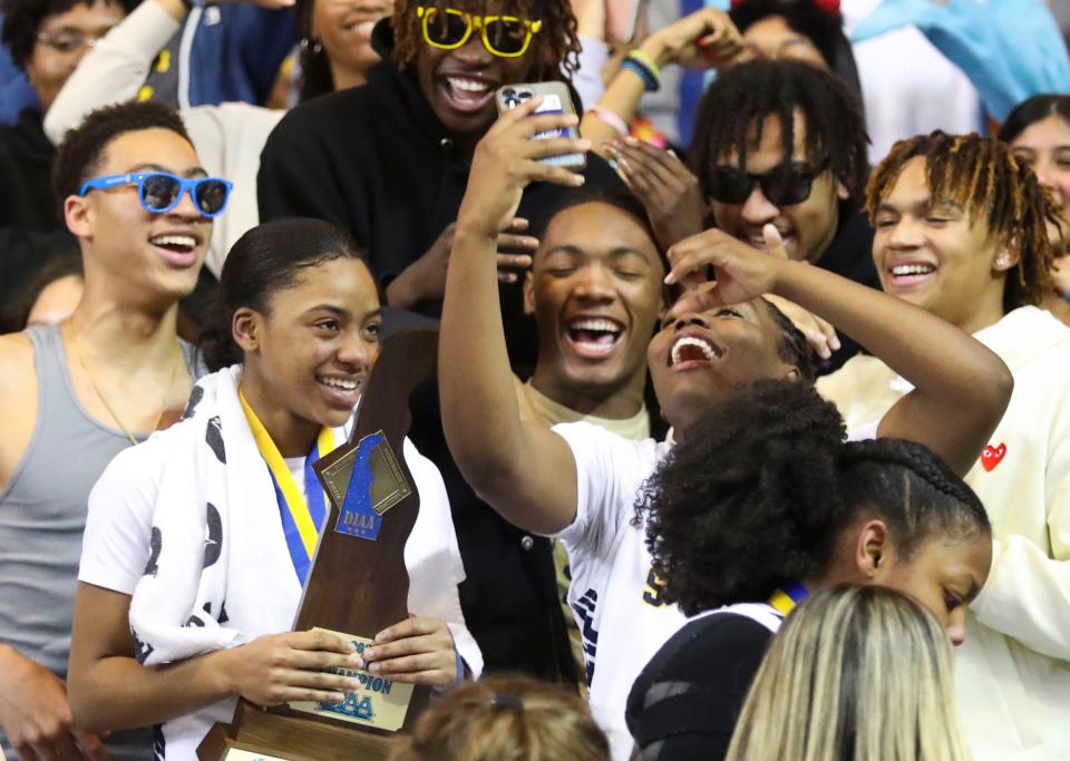 Sanford's Zy Kilgoe (with trophy) joins a celebratory selfie by teammate Dallas Pierce in the stands with their classmates after the Warriors' 58-46 win against Ursuline in the DIAA state tournament championship game at the Bob Carpenter Center, Friday, March 10, 2023.