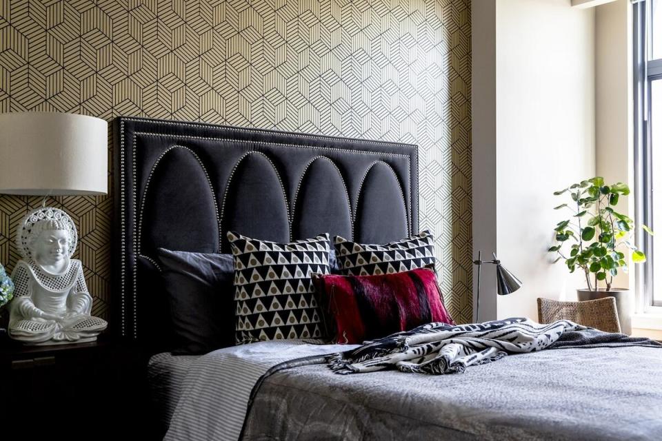 A geometric wallpaper accent wall, curved nailhead detailing on the headboard and a medley of patterns and textures on the bed form a cozy retreat