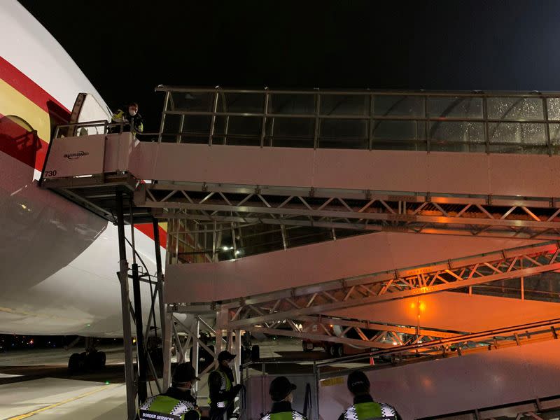 Canada Border Services Agency (CBSA) agents await passengers disembarking on a walkway from a cargo plane at Vancouver airport