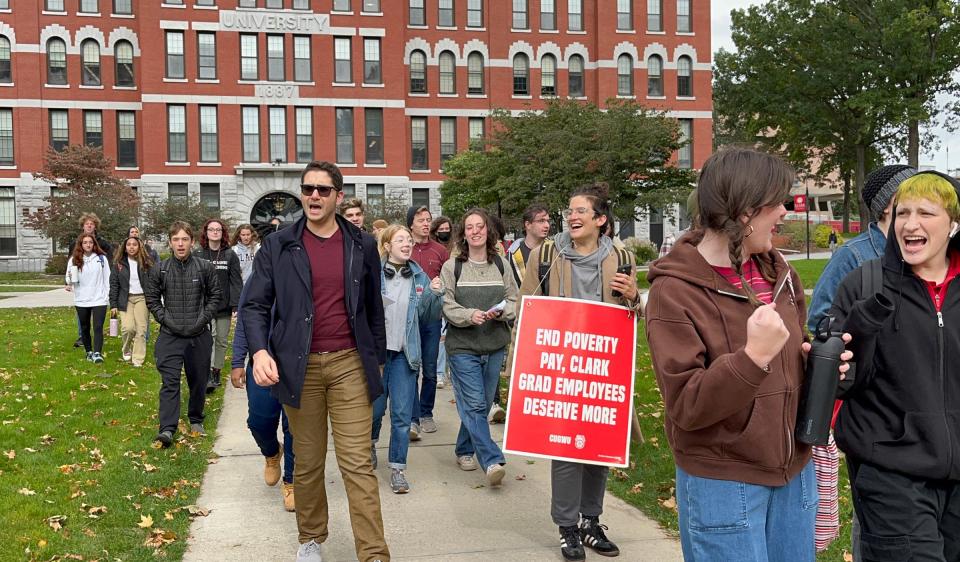 Striking Clark University graduate student workers march off campus holding signs and chanting Monday in Worcester.