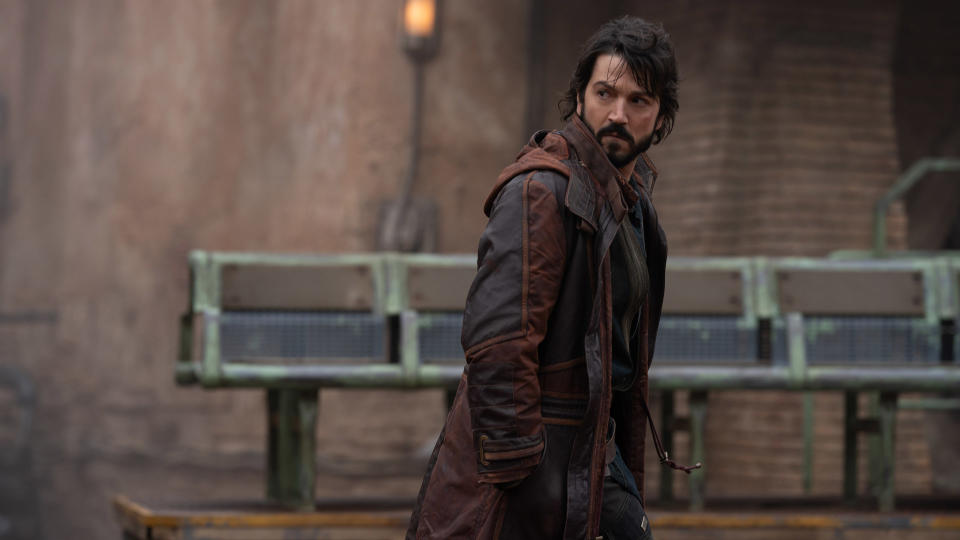 Cassian Andor looks behind him as he walks through Ferrix's main city in Andor on Disney Plus