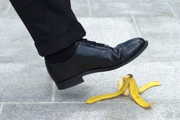 A black shoe about to step on a banana peel.