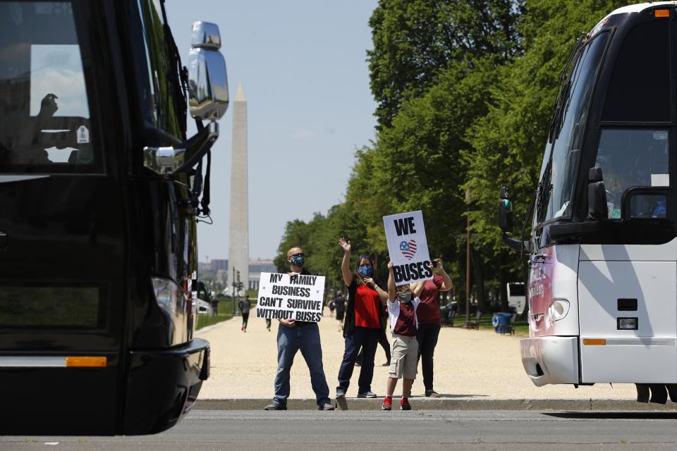FILE - In this May 13, 2020, file photo, Grant Curry, left, a tour company operator from Indianapolis, and his son Gavin, 10, wave signs in support of bus and motor coach operators circling National Mall in Washington during a rally to raise awareness of the industry in the wake of the coronavirus outbreak. America's private buses are ground to a halt, and members of the industry say they need federal assistance to help the country get back to work and play. (AP Photo/Patrick Semansky, File)