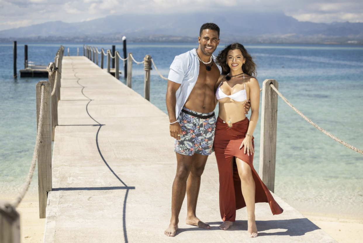 Nicole Jacky and Kendall Washington stand arm-in-arm wearing beach attire on a pier.