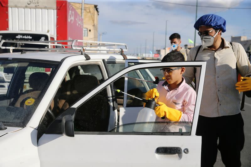 A volunteer and his son wearing a protective face masks= and gloves, following the outbreak of coronavirus disease (COVID-19), disinfect a car in Qom