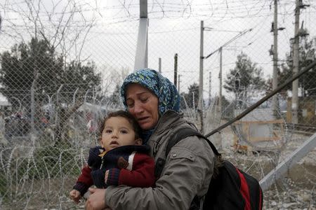 A migrant holding a child cries next to a border fence at the Macedonian-Greek border in Gevgelija, Macedonia February 24, 2016. REUTERS/Marko Djurica