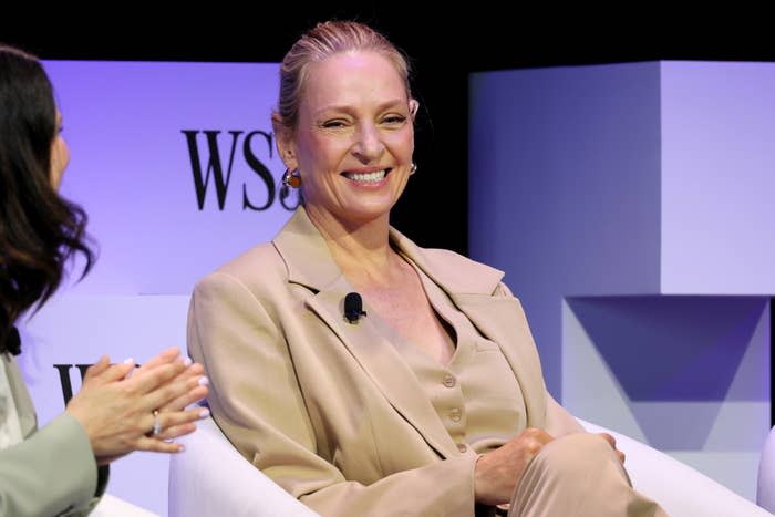 I don’t know who this is, but the person is seated, smiling, wearing a beige suit, and speaking at a panel event